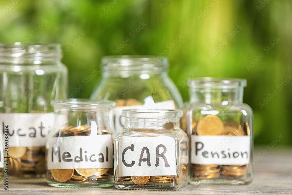 Coins for different needs in glass jars on table outdoors. Money savings concept Coins for different needs in glass jars on table outdoors. Money savings concept