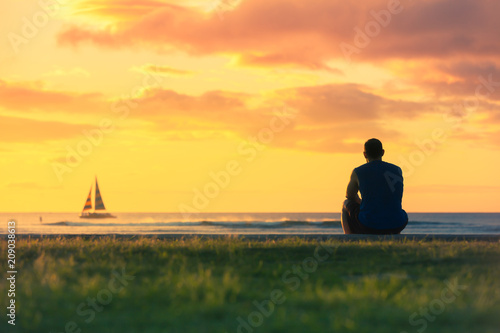 Man relaxing by the sea watching the colourful sunset and sail boats go by. © kieferpix