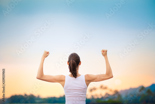 People, power, strength, and determination.  Strong woman flexing her muscles against sunset. 