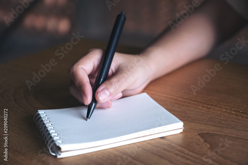 Closeup image of a hand writing down on a white blank notebook on wooden table