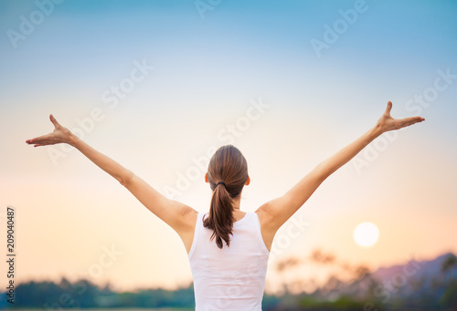 Young woman raising her arms up against the sunset feeling free. Happiness and joy concept. 
