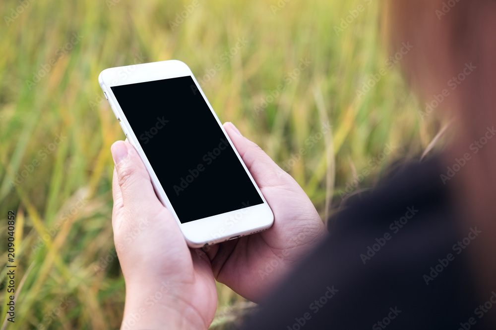 Mockup image of a woman holding white mobile phone with blank black desktop screen with blur green nature background