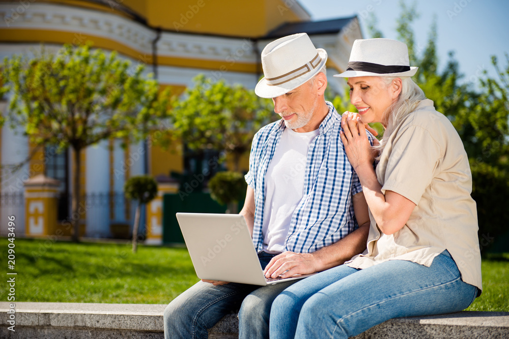 Portrait of cheerful lovely couple sitting outdoor using laptop making online shopping watching video having video-call. Connection communication social networks concept