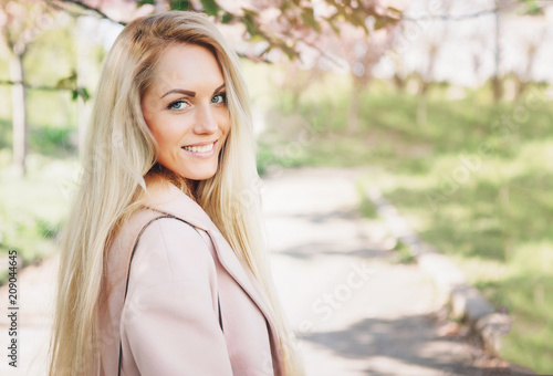 Woman with  long blond hair in the garden with flowers. Beautiful girl on a sunny day.