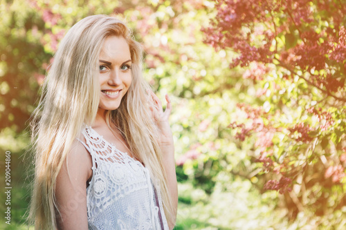 Woman with long blond hair in the garden with flowers. Beautiful girl on a sunny day.