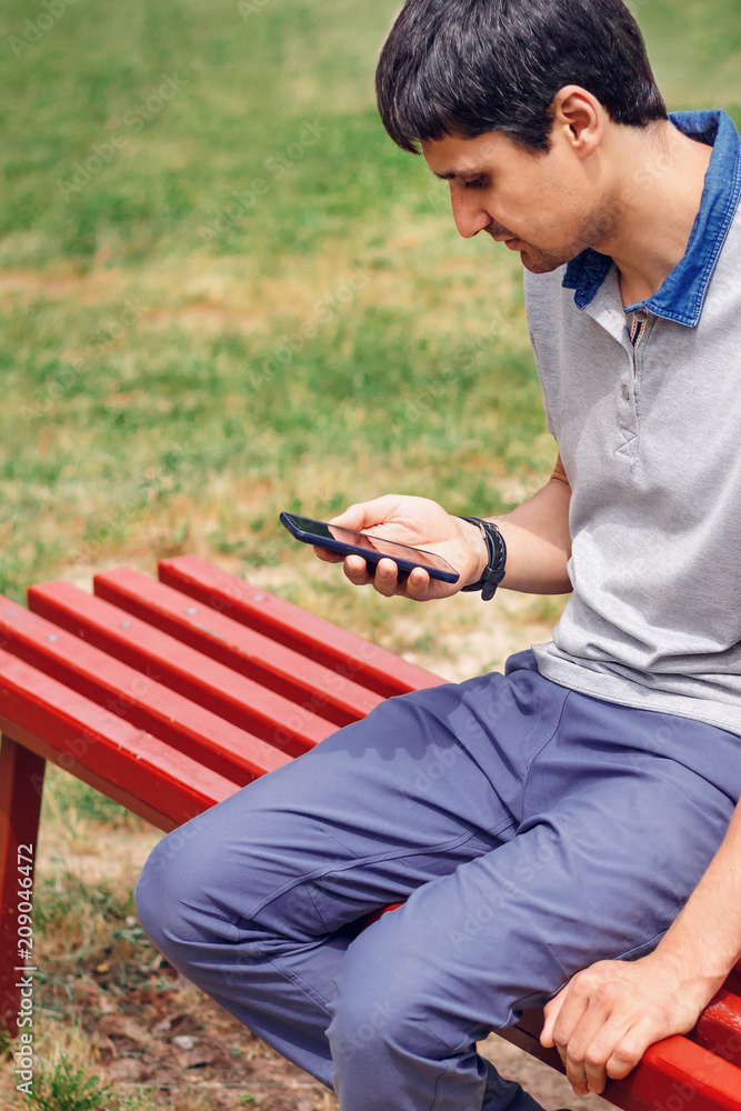 Obraz premium the man is sitting on a bench and using a smartphone with a gray display on the city street, close-up