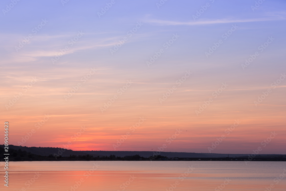 the sun has set by the coastline, the sky is illuminated by the sun, a beautiful sky with color gradients and gentle clouds, a reflection of the sky in the water