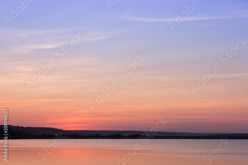 the sun has set by the coastline, the sky is illuminated by the sun, a beautiful sky with color gradients and gentle clouds, a reflection of the sky in the water