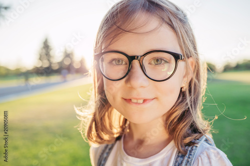 Girl looking at camera and smiling in nature against sunset. Summer leisure. Girl in glasses with black rim.