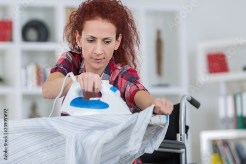 pretty redhead woman sitting on wheelchair and ironing