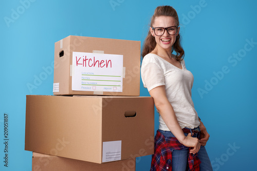 happy modern woman standing next to cardboard boxes on blue