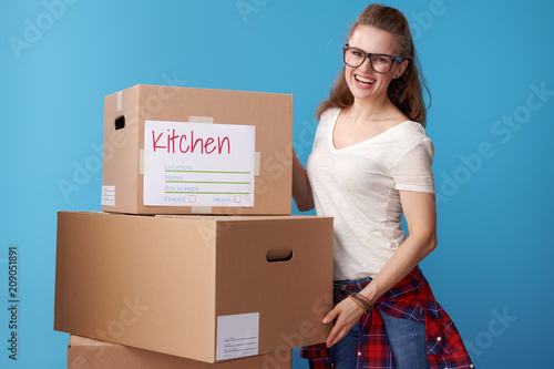 happy young woman standing next to cardboard boxes on blue