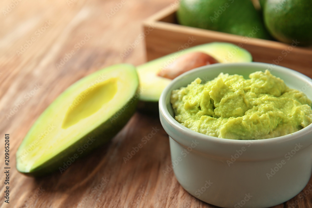 Bowl with tasty guacamole and ripe avocados on wooden table Bowl with tasty guacamole and ripe avocados on wooden table