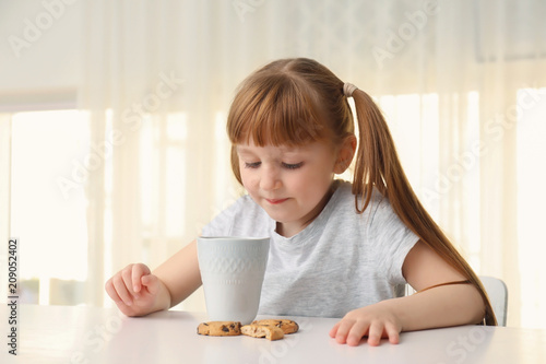 Cute little girl with cup of hot cocoa drink and cookies at home