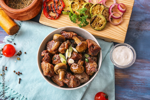 Bowl with pieces of shish-kebab and mushrooms on table