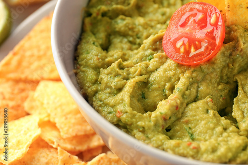Bowl with delicious guacamole and nachos on plate, closeup