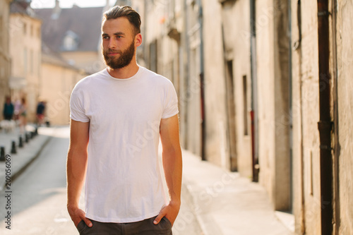 Hipster handsome male model with beard wearing white blank t-shirt with space for your logo or design in casual urban style
