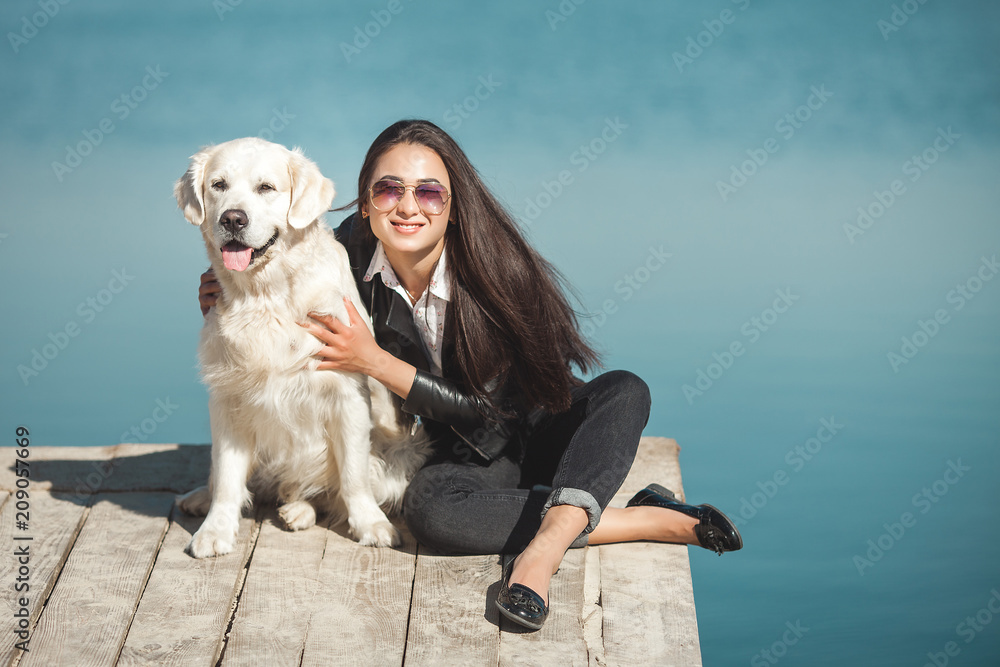 Young attractive woman sitting at the pier with her dog. Best friends outdoors