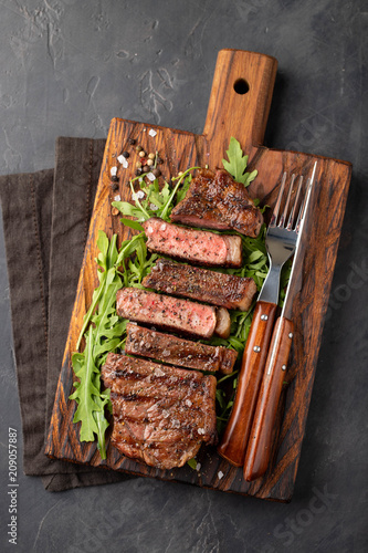 Closeup ready to eat steak new York beef breeds of black Angus with herbs, garlic and butter on a wooden Board. The finished dish for dinner on a dark stone background. Top view