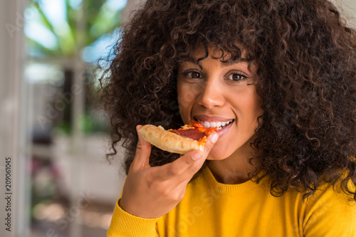African american woman ready to eat pepperoni pizza slice with a confident expression on smart face thinking serious