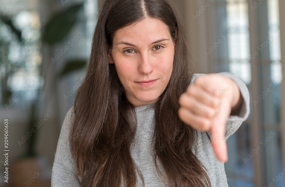 Young beautiful woman at home looking unhappy and angry showing rejection and negative with thumbs down gesture. Bad expression.