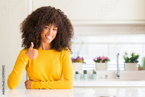 African american woman wearing yellow sweater at kitchen doing happy thumbs up gesture with hand. Approving expression looking at the camera with showing success.