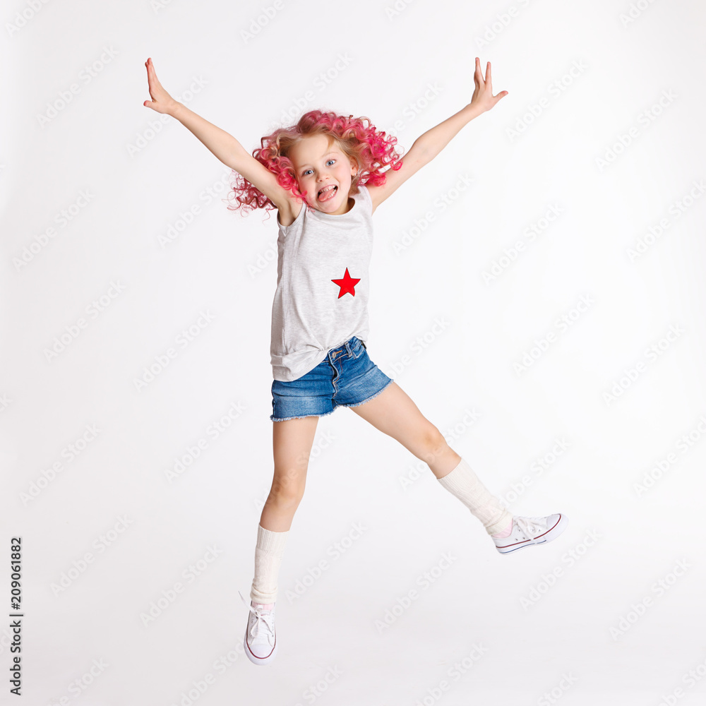Colored wavy hairs. Little modern hipster girl in fashion clothes, jumping in studio and showing tongue Colored wavy hairs. Little modern hipster girl in fashion clothes, jumping in studio and showing tongue