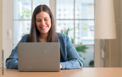 Young woman using laptop at home with a happy face standing and smiling with a confident smile showing teeth