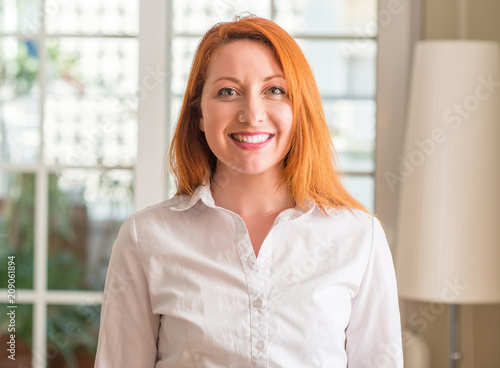 Redhead woman wearing white shirt at home with a happy face standing and smiling with a confident smile showing teeth Free Download Redhead woman wearing white shirt at home with a happy face standing and smiling with a confident smile showing teeth - GFXLoad