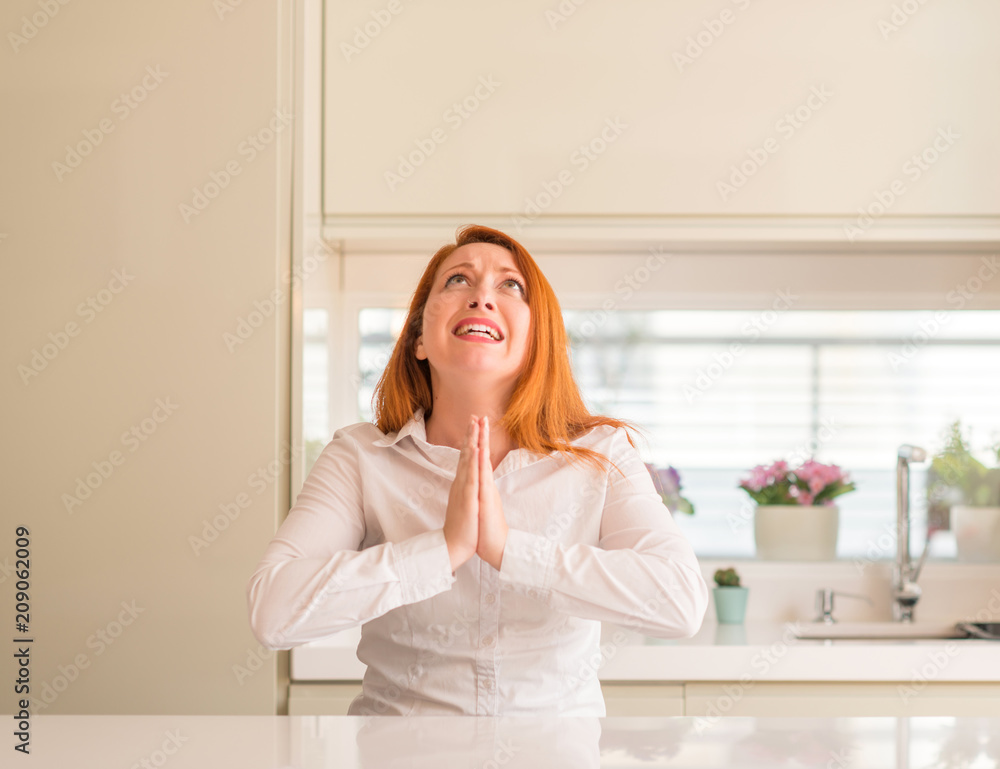 Redhead woman at kitchen begging and praying with hands together with hope expression on face very emotional and worried. Asking for forgiveness. Religion concept. Redhead woman at kitchen begging and praying with hands together with hope expression on face very emotional and worried. Asking for forgiveness. Religion concept.
