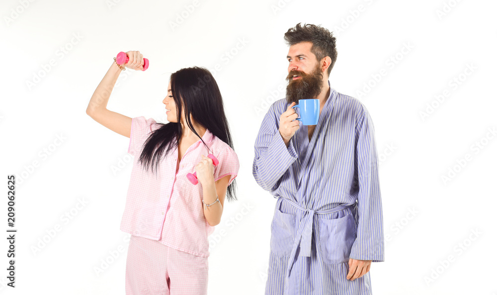 Couple in love in pajama, bathrobe stand isolated on white background. Girl with dumbbell, man with coffee cup. Couple, family on sleepy faces, full of energy. Alternative lifestyle concept. Couple in love in pajama, bathrobe stand isolated on white background. Girl with dumbbell, man with coffee cup. Couple, family on sleepy faces, full of energy. Alternative lifestyle concept.