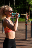 Photo of sports woman wearing sunglasses with bottle of water near horizontal bar in park