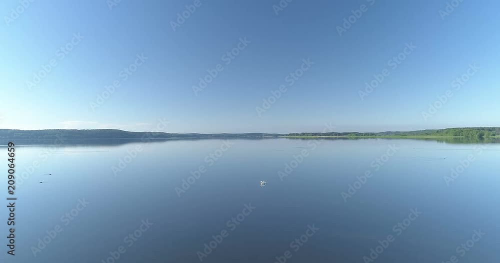 Low aerial flight over the edge of tranquil lake with lone swan in the middle Low aerial flight over the edge of tranquil lake with lone swan in the middle