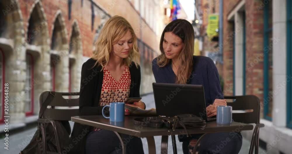 Lovely blonde woman with girlfriend using smartphone to locate destination in Bruges, Belgium, Two cute young adult women looking at cell phone with map in European street cafe, 4k Lovely blonde woman with girlfriend using smartphone to locate destination in Bruges, Belgium, Two cute young adult women looking at cell phone with map in European street cafe, 4k