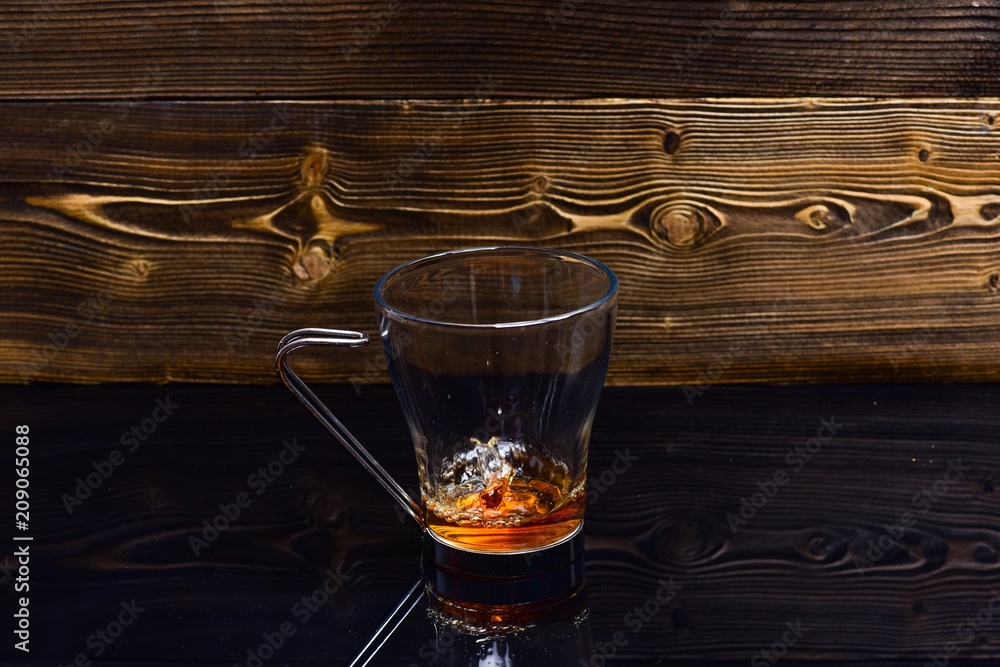 Cup pouring with water or tea with splashes on dark wooden background. Glass with tea pouring with liquid with splashes and drops of water. Brewing tea concept Cup pouring with water or tea with splashes on dark wooden background. Glass with tea pouring with liquid with splashes and drops of water. Brewing tea concept