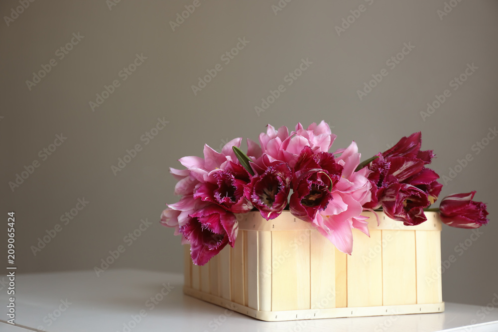 Box with beautiful tulips on table against grey background