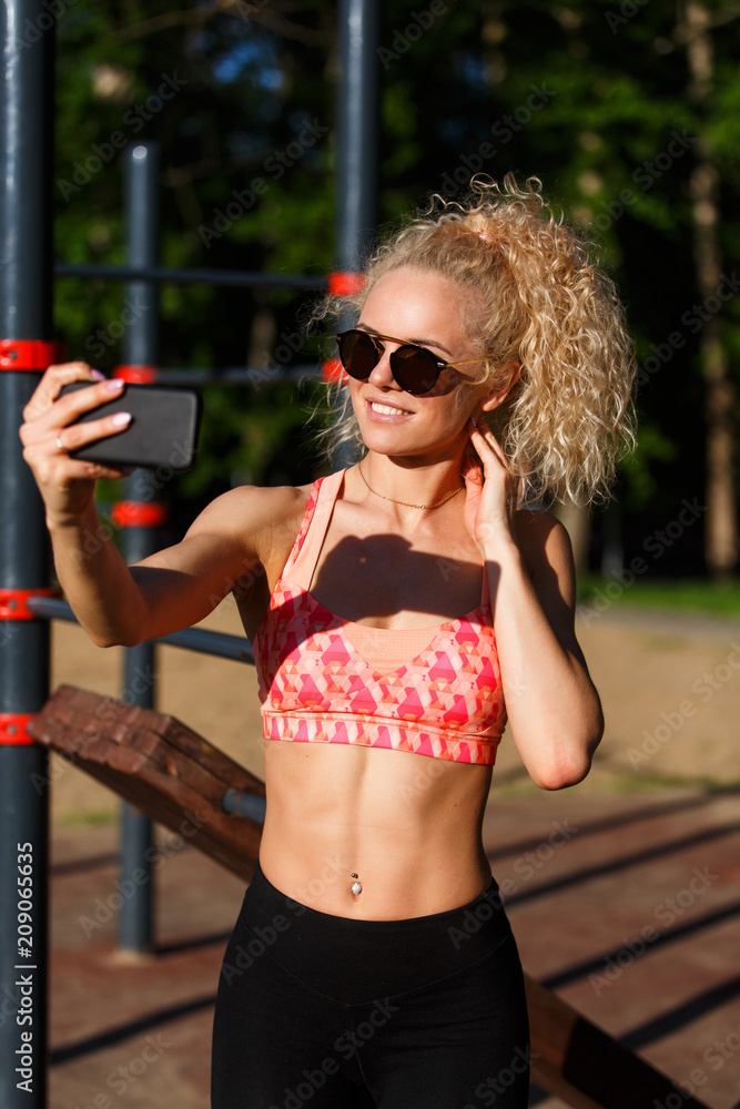 Photo of smiling sports woman wearing sunglasses doing selfie in park