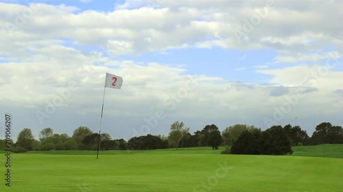 Green golf course with white flag and the hole. Sport, relax, recreation and leisure concept. Summer landscape on a bright sunny day with cloudy sky