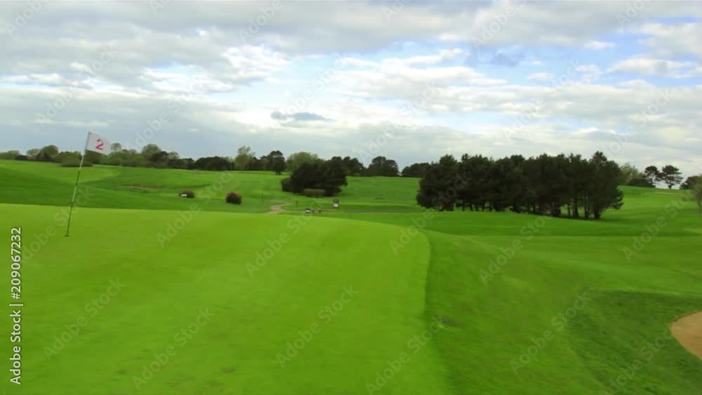 Green golf course with white flag and the hole. Sport, relax, recreation and leisure concept. Summer landscape on a bright sunny day with cloudy sky Green golf course with white flag and the hole. Sport, relax, recreation and leisure concept. Summer landscape on a bright sunny day with cloudy sky
