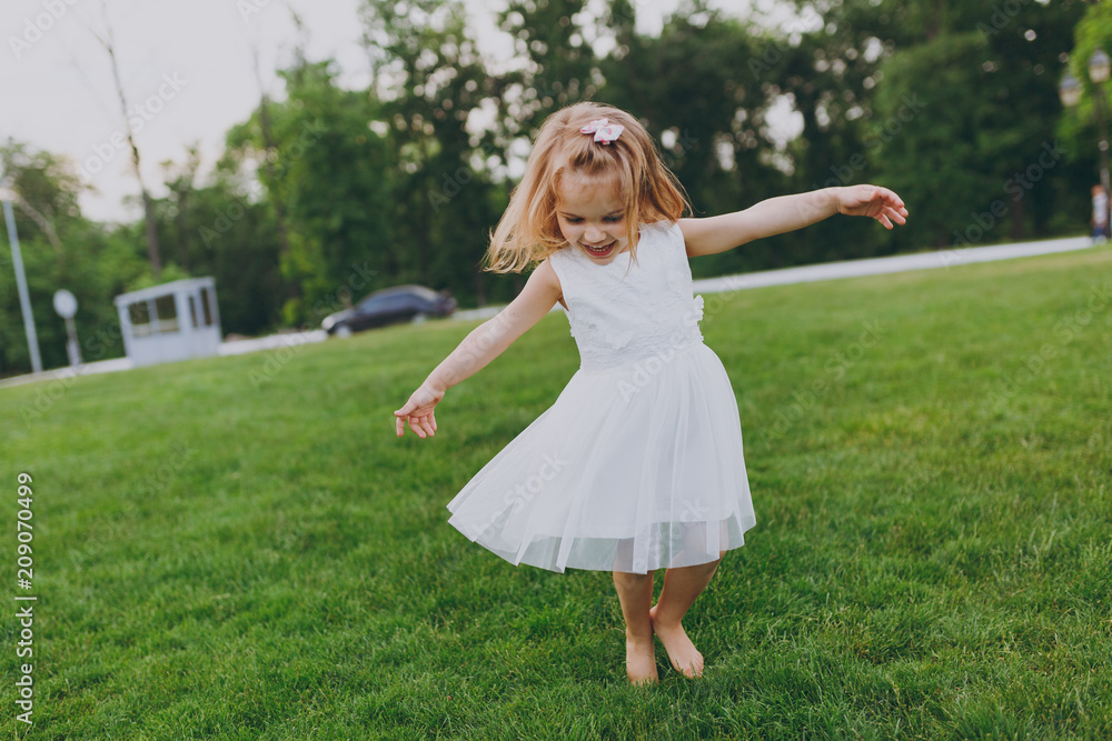 Pretty little cute child baby girl in light dress circling around and have fun on green grass lawn in park. Mother, little kid daughter. Mother's Day, love family, parenthood, childhood concept. Pretty little cute child baby girl in light dress circling around and have fun on green grass lawn in park. Mother, little kid daughter. Mother's Day, love family, parenthood, childhood concept.