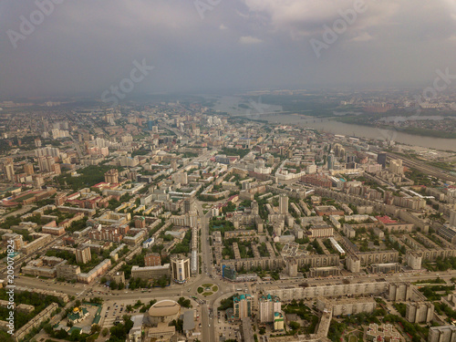 Aerial view of square in the city with roundabout traffic, streets and buildings with green trees. A lot of buildings in Novosibirsk with cloudy weather.