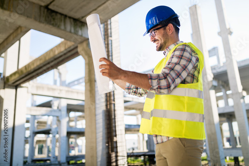 Portrait of male site contractor engineer with hard hat holding blue print paper © NDABCREATIVITY