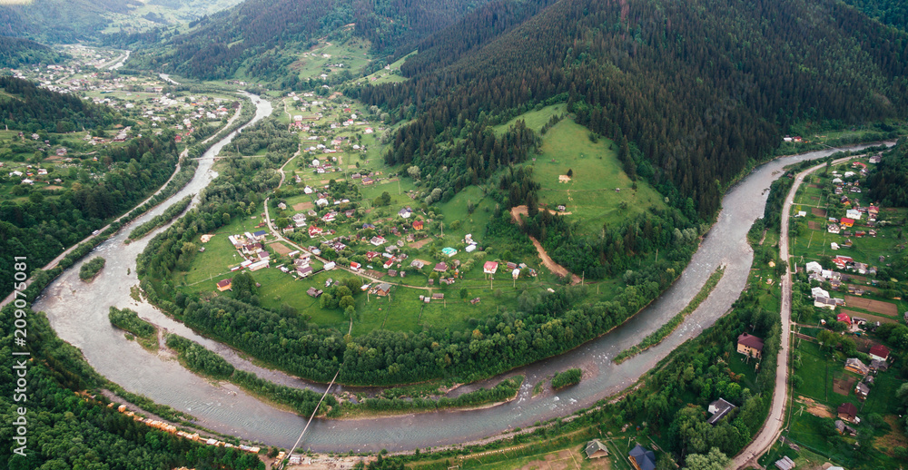 Aerial View: mountain river in the form of meander  flows through the mountains through the picturesque village of the Carpathians