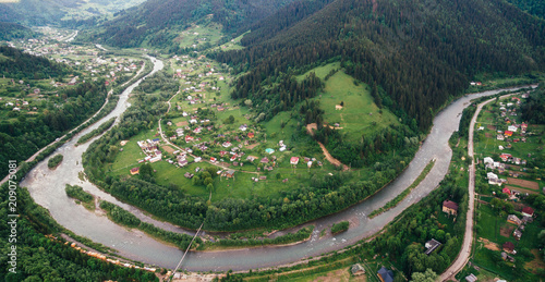 Aerial View: mountain river in the form of meander flows through the mountains through the picturesque village of the Carpathians