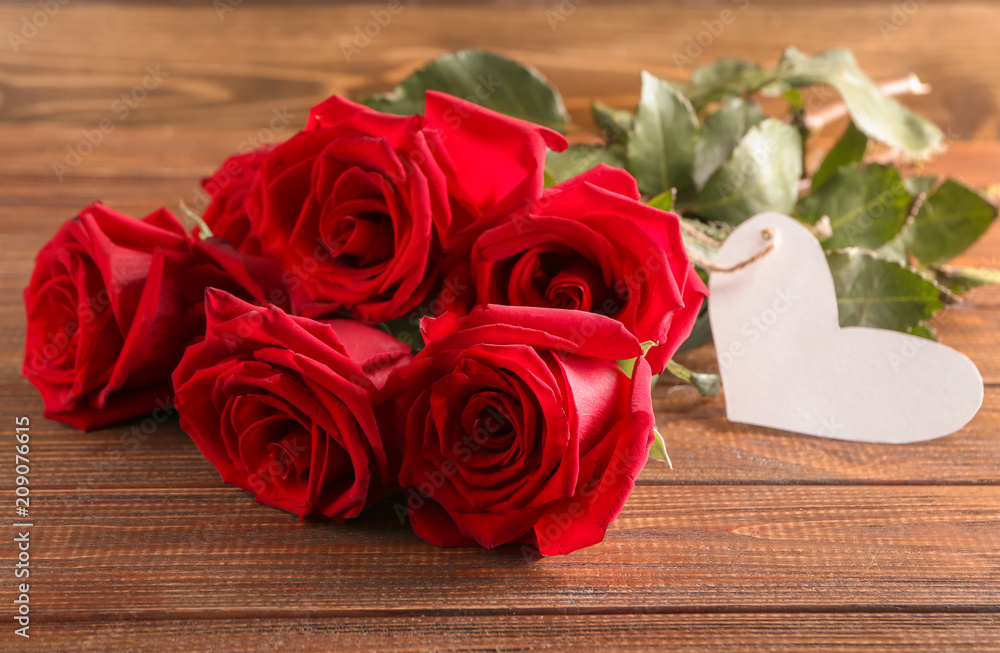 Beautiful roses with heart-shaped tag on wooden background