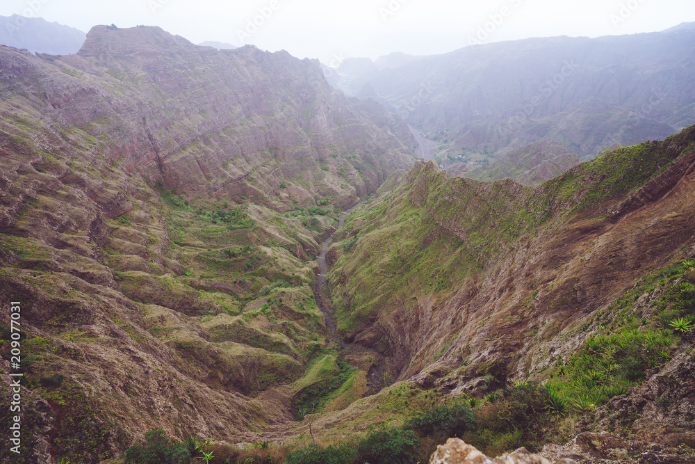 Breathtaking panorama of a steep gorge with haze riverbed and lush green vegetation in the valley of Delgadinho mountain ridge. Santo Antao, Cape Verde