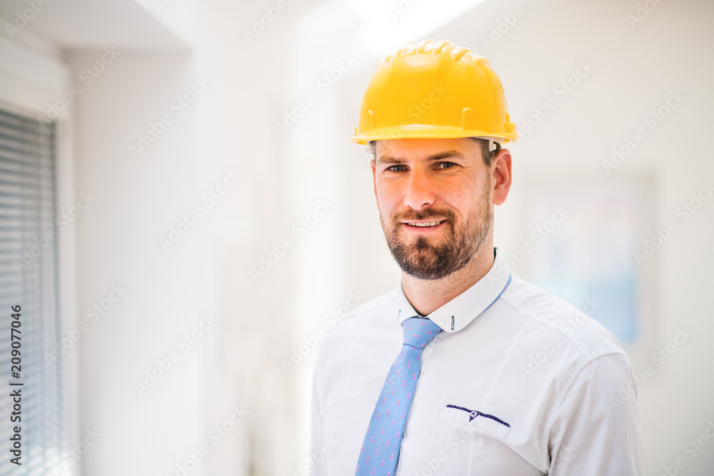 A young engineer or architect with white shirt, tie and helmet in a room. A young engineer or architect with white shirt, tie and helmet in a room.