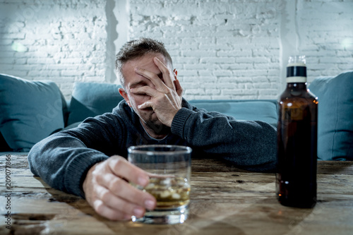 young drunk man depressed and sad drinking whiskey at home photo