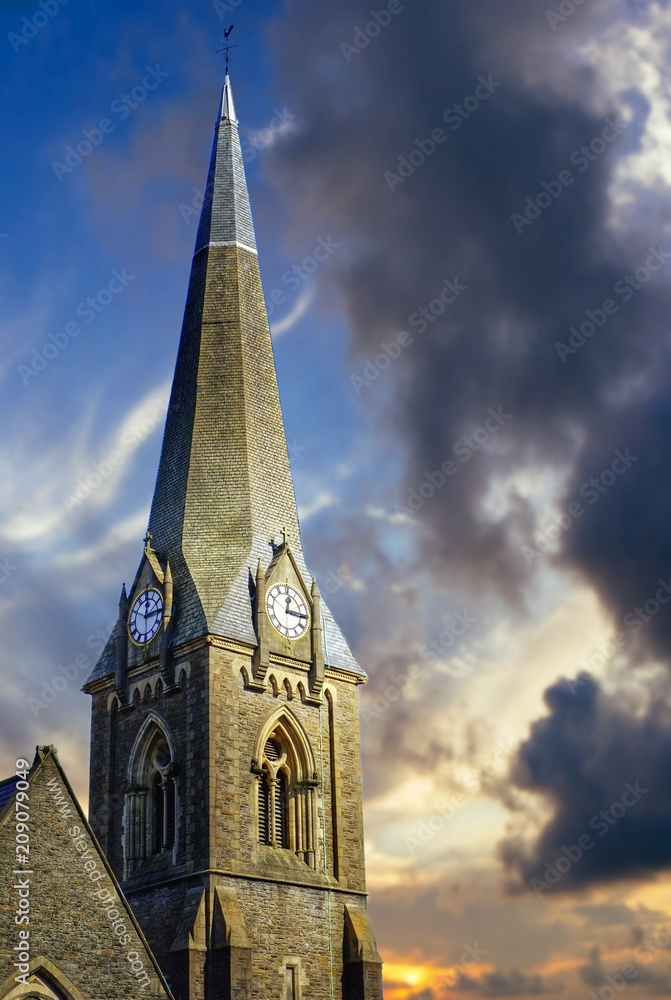 Church steeple with clock faces on each side beneath dramatic early evening sky.