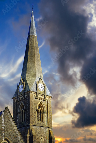 Church steeple with clock faces on each side beneath dramatic early evening sky. © pepgooner